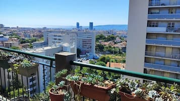 A balcony with potted plants, a view of a cityscape, and a clear blue sky.