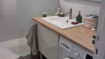 A modern bathroom with a shower, sink, mirror, and built-in washing machine.