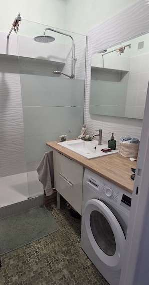 A modern bathroom with a shower, sink, mirror, and built-in washing machine. - Bed and Breakfast for Solo Female Travelers (Marseille)