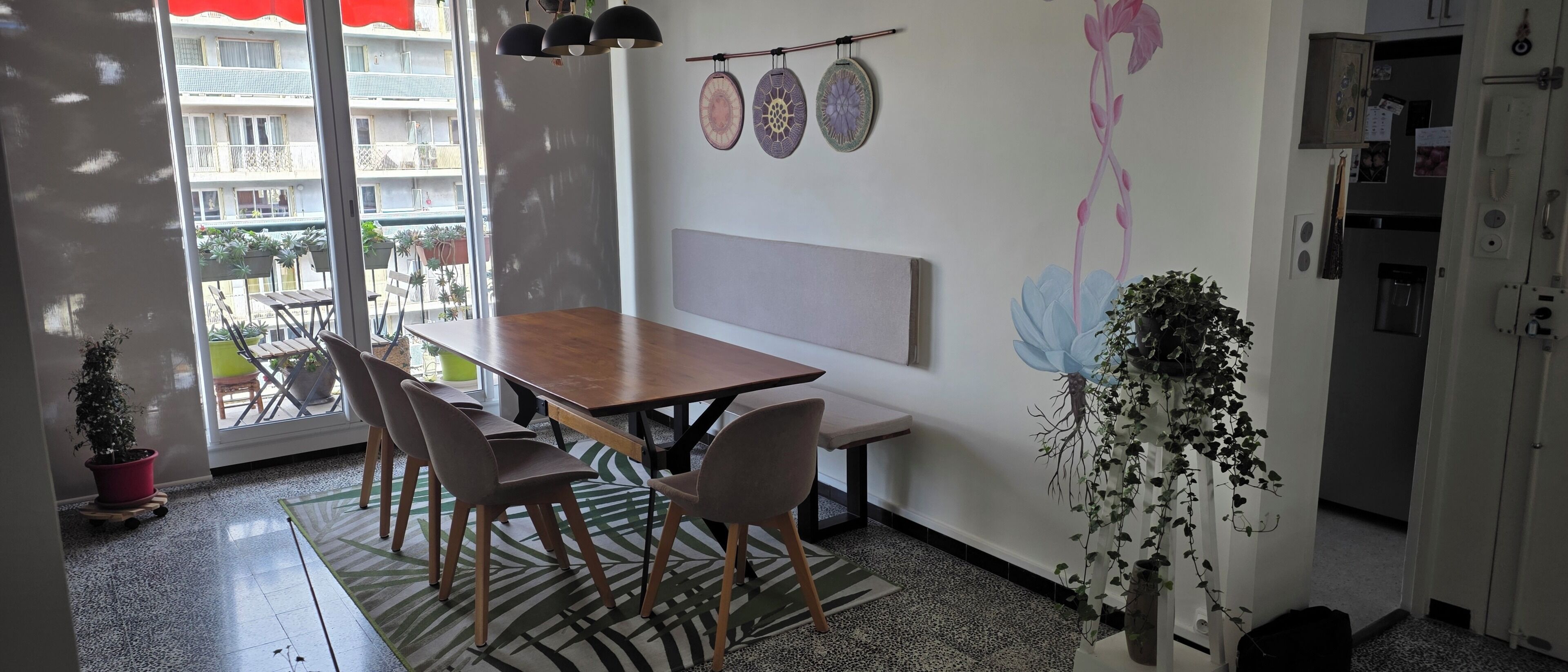A dining area with a wooden table and chairs, a bench, a wall-mounted light fixture, and a view through a glass door.