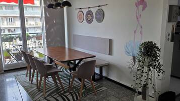 A dining area with a wooden table and chairs, a bench, a wall-mounted light fixture, and a view through a glass door.