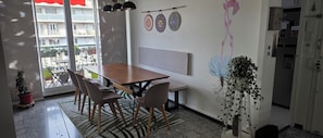 A dining area with a wooden table and chairs, a bench, a wall-mounted light fixture, and a view through a glass door. - Bed and Breakfast for Solo Female Travelers (Marseille)