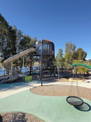 A playground with a slide, climbing structures, and swings. - Lovely Lake Treeby Home | 1 Min to Park & Playgrounds (Treeby)