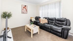 Een moderne woonkamer met een zwarte leren bank, een houten salontafel, een potplant en een lijst met kunstwerk aan de muur.