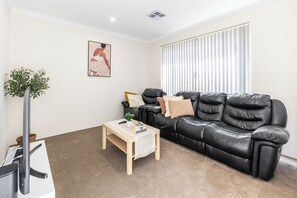 A modern living room with a black leather sofa, a wooden coffee table, a potted plant, and a framed artwork on the wall. - Lovely Lake Treeby Home | 1 Min to Park & Playgrounds (Treeby)