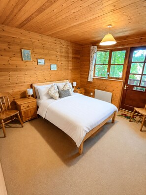 Ein Schlafzimmer einer Holzhütte mit einem Bett, Nachttischen, einem Sessel und einem Fenster mit Vorhängen.