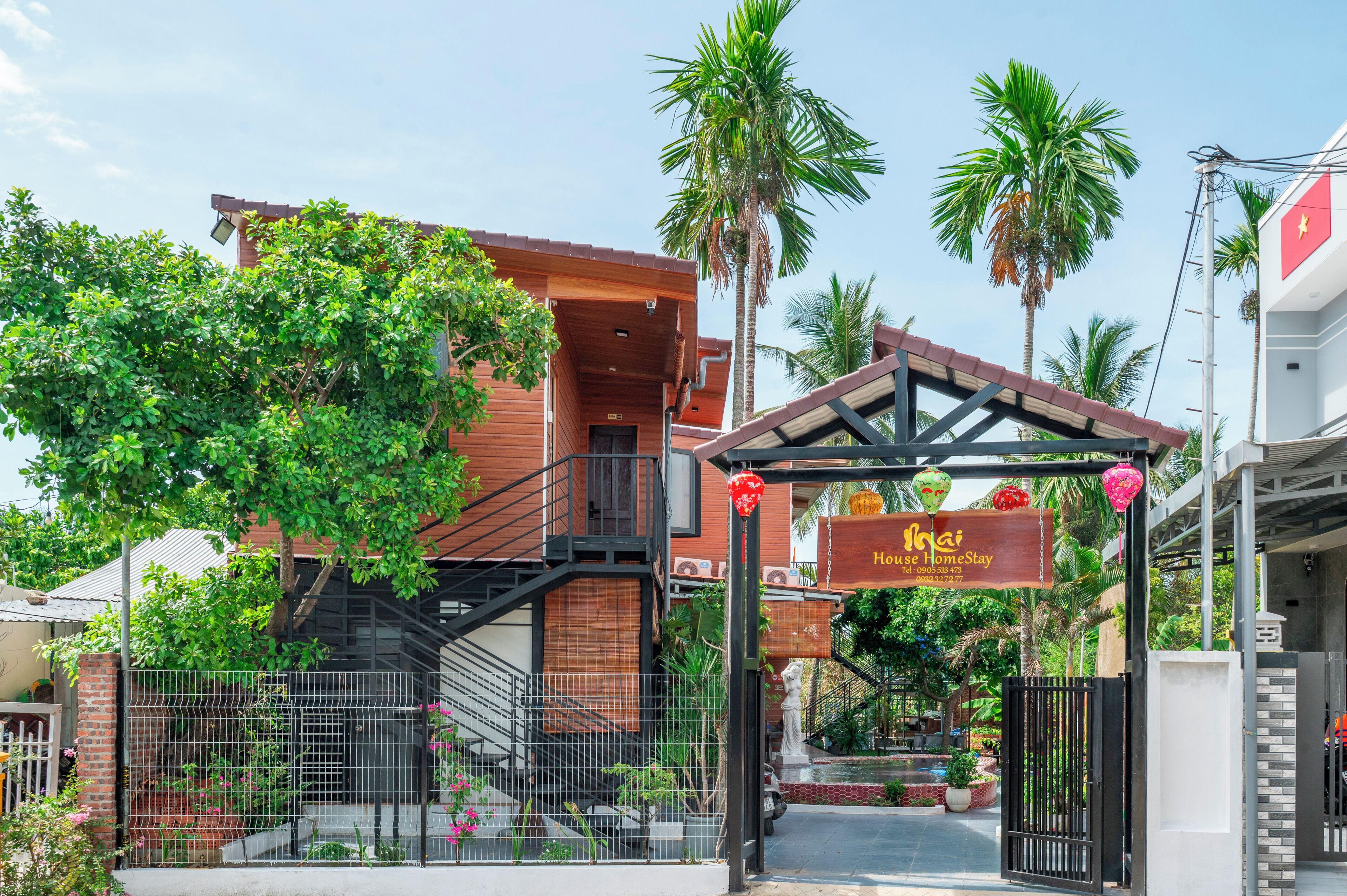 A hotel entrance with a gated driveway, a staircase leading to the entrance, and a signboard with the hotel's name and contact information.