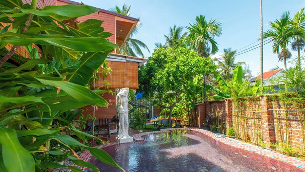 A swimming pool with a tiled edge, surrounded by lush greenery and a bamboo fence. - Mai House Homestay (Da Nang)