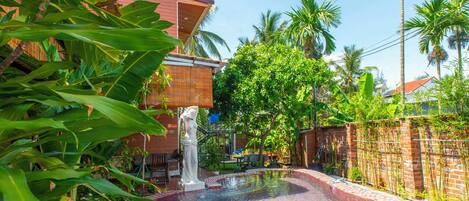 A swimming pool with a tiled edge, surrounded by lush greenery and a bamboo fence.