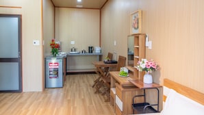A compact kitchen with a refrigerator, stove, and sink. There is a dining table with chairs and a small cabinet. - Mai House Homestay (Da Nang)