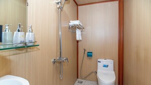 A small, compact bathroom with a shower, toilet, and a glass shelf with toiletries. - Mai House Homestay (Da Nang)