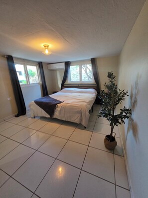 A bedroom with a bed, a potted plant, a window, and an air conditioning unit. - Green haven studio (Oranjestad)