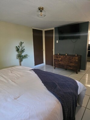 A bedroom with a bed, a dresser, a television mounted on the wall, and a ceiling light fixture. - Green haven studio (Oranjestad)