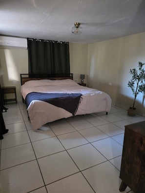 A bedroom with a bed, a nightstand, a lamp, a ceiling fan, and a potted plant. - Green haven studio (Oranjestad)