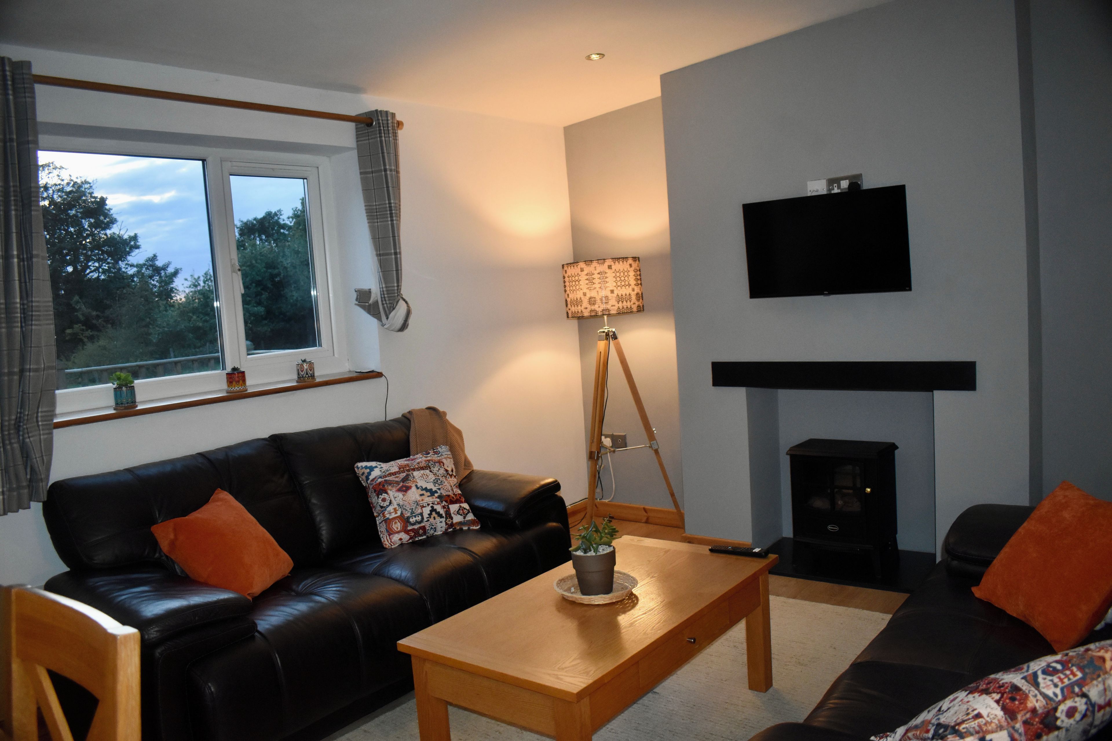 A living room with a black leather sofa, a wooden coffee table, a floor lamp, a flat-screen TV, and a fireplace.