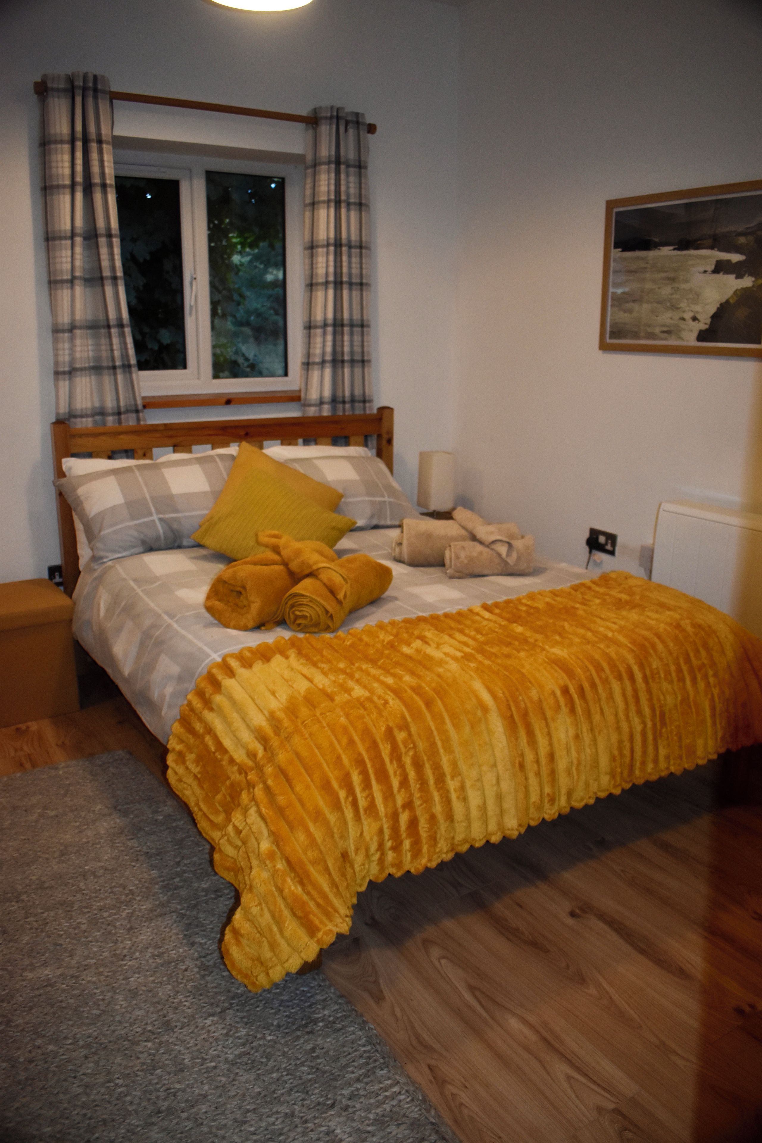 A bedroom with a bed, a window, curtains, a painting, and a radiator.
