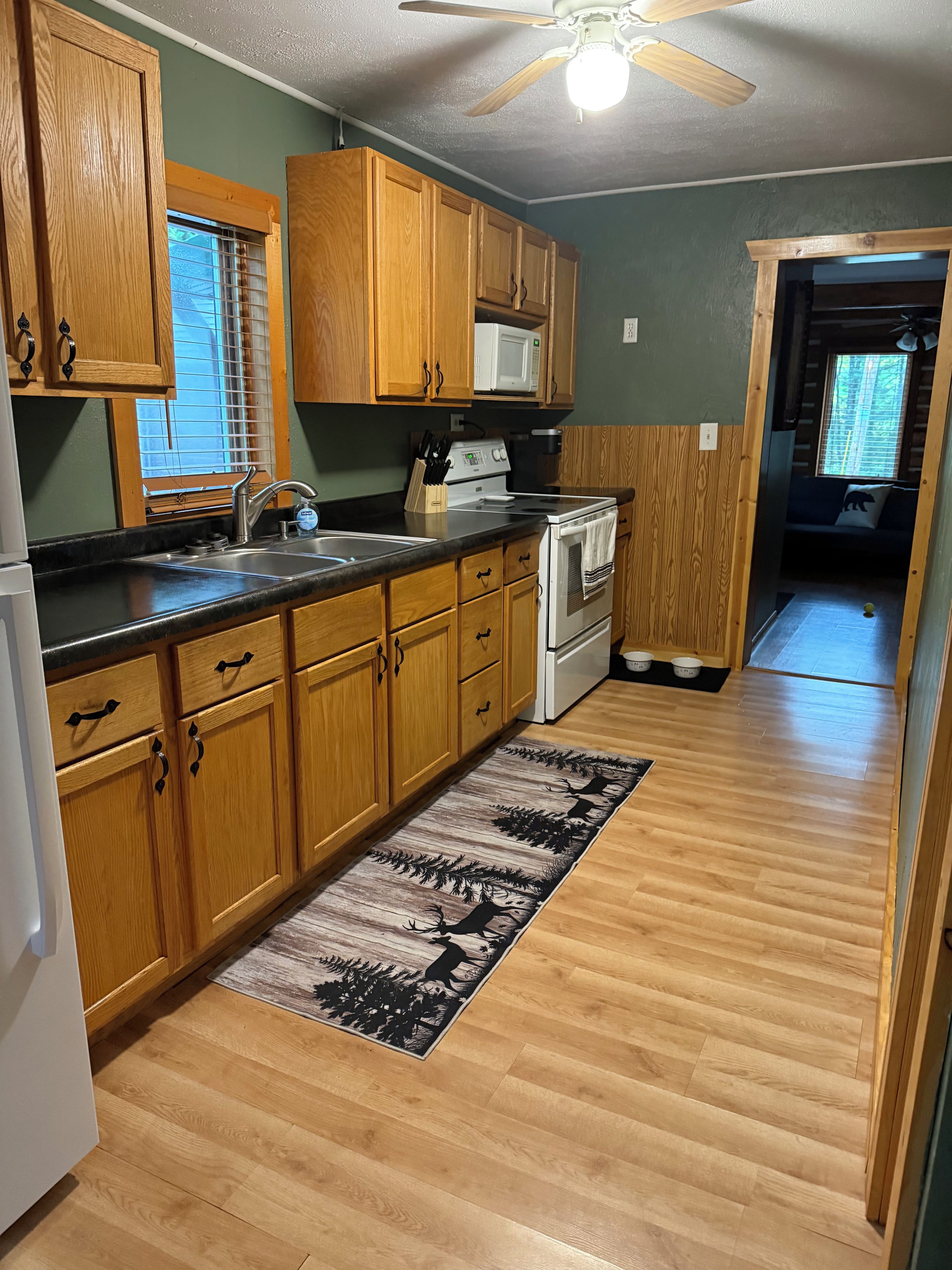 A kitchen with wooden cabinets, a microwave, a stove, and a window with blinds.