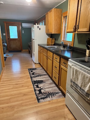 A kitchen with wooden cabinets, a refrigerator, a stove, and a window with a view. - 7 Pines Cabin Hunt, Fish & Ride (Mountain)