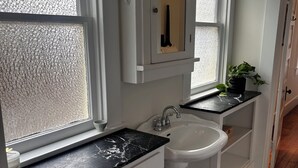 Un baño con un lavamanos blanco, encimera de mármol, una planta en maceta y suelo de baldosas blancas y negras.