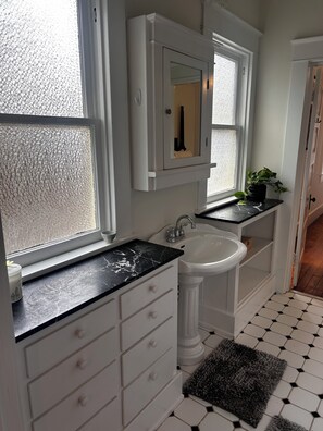 A bathroom with a white sink, a marble countertop, a potted plant, and a black and white tiled floor. - Cozy 2-bedroom house in peaceful Monroe close to restaurants and more! (Monroe)
