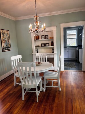 A dining area with a white round table and chairs, a chandelier, and a kitchen visible through an open door. - Cozy 2-bedroom house in peaceful Monroe close to restaurants and more! (Monroe)
