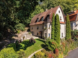 A two-story house with a sloped roof, a front porch, and a garden with various plants and a bench. - Wonderful 9-bedroom villa in Karlovy Vary for your getaway (Karlovarský kraj)