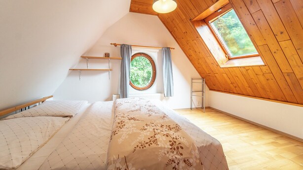 Een slaapkamer met een schuine hemel, een dakraam, een bed met een bloemenbedekking en een radiator.