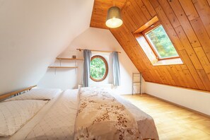 Een slaapkamer met een schuine hemel, een dakraam, een bed met een bloemenbedekking en een radiator.