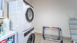 Een wasruimte met een witte wasmachine, een droogrek en diverse schoonmaakmiddelen.