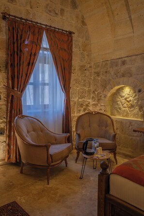 Una habitación con dos sillones, una mesita con objetos, una cama y una pared de piedra con chimenea.