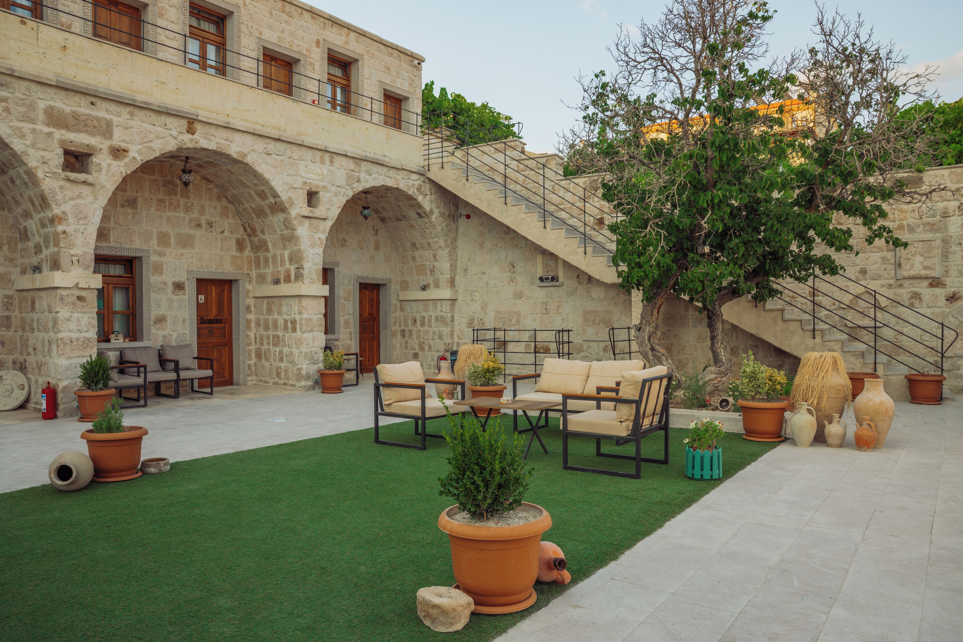 A courtyard with stone arches, outdoor furniture, potted plants, and a staircase leading to an upper level.