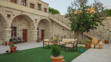 A courtyard with stone arches, outdoor furniture, potted plants, and a staircase leading to an upper level.