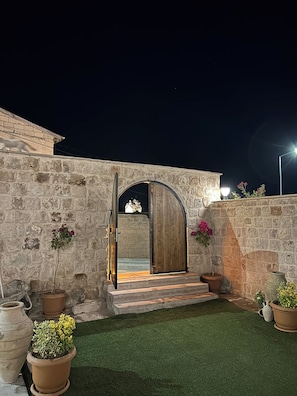 A stone wall entrance with a wooden door, potted plants, and a small set of steps leading to a dark interior. - Cappa Hisar Cave House (Ortahisar)