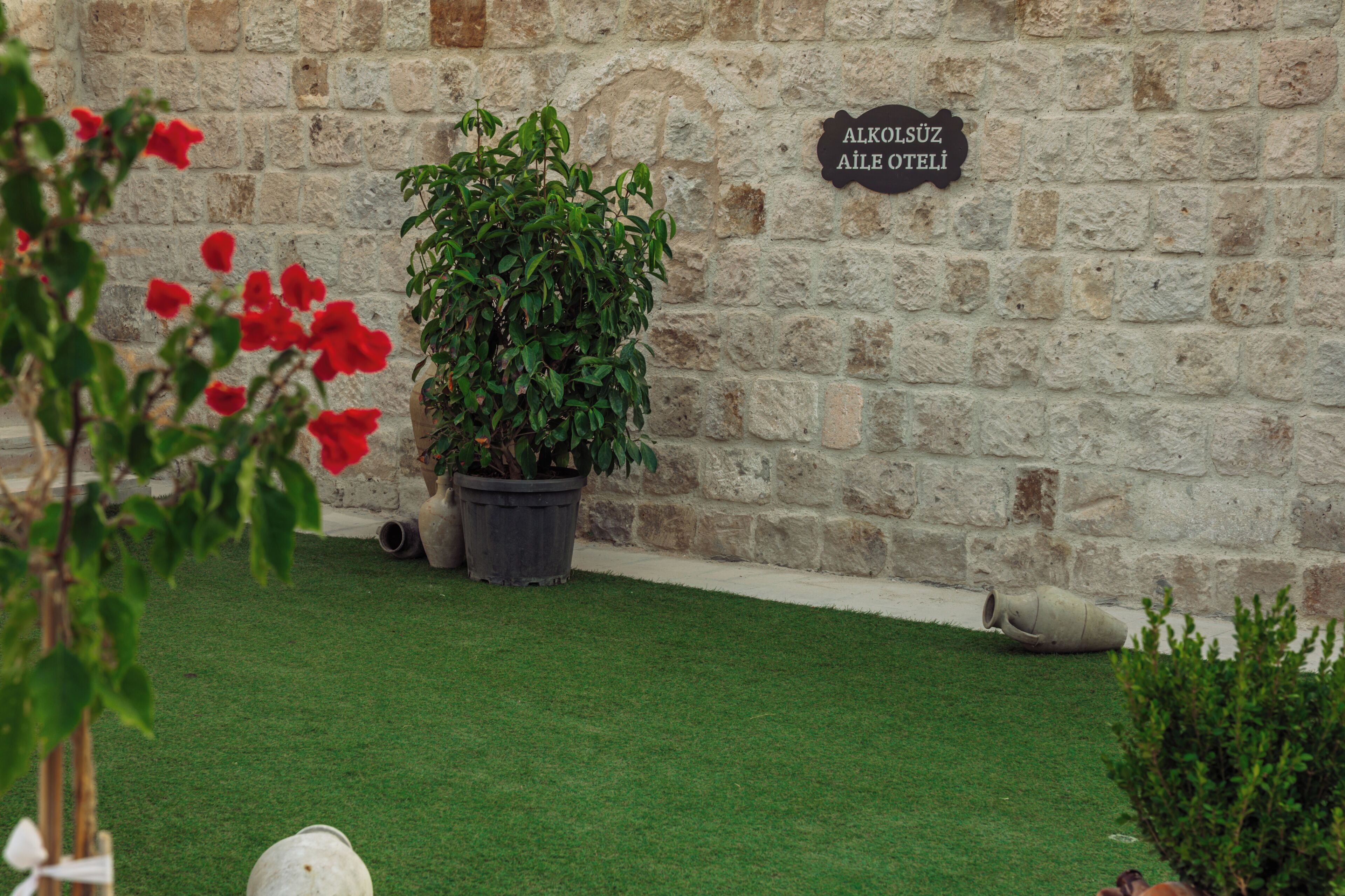 A stone wall with a sign for 'Alkol Süz Aile Otelleri' and a potted plant in the foreground.