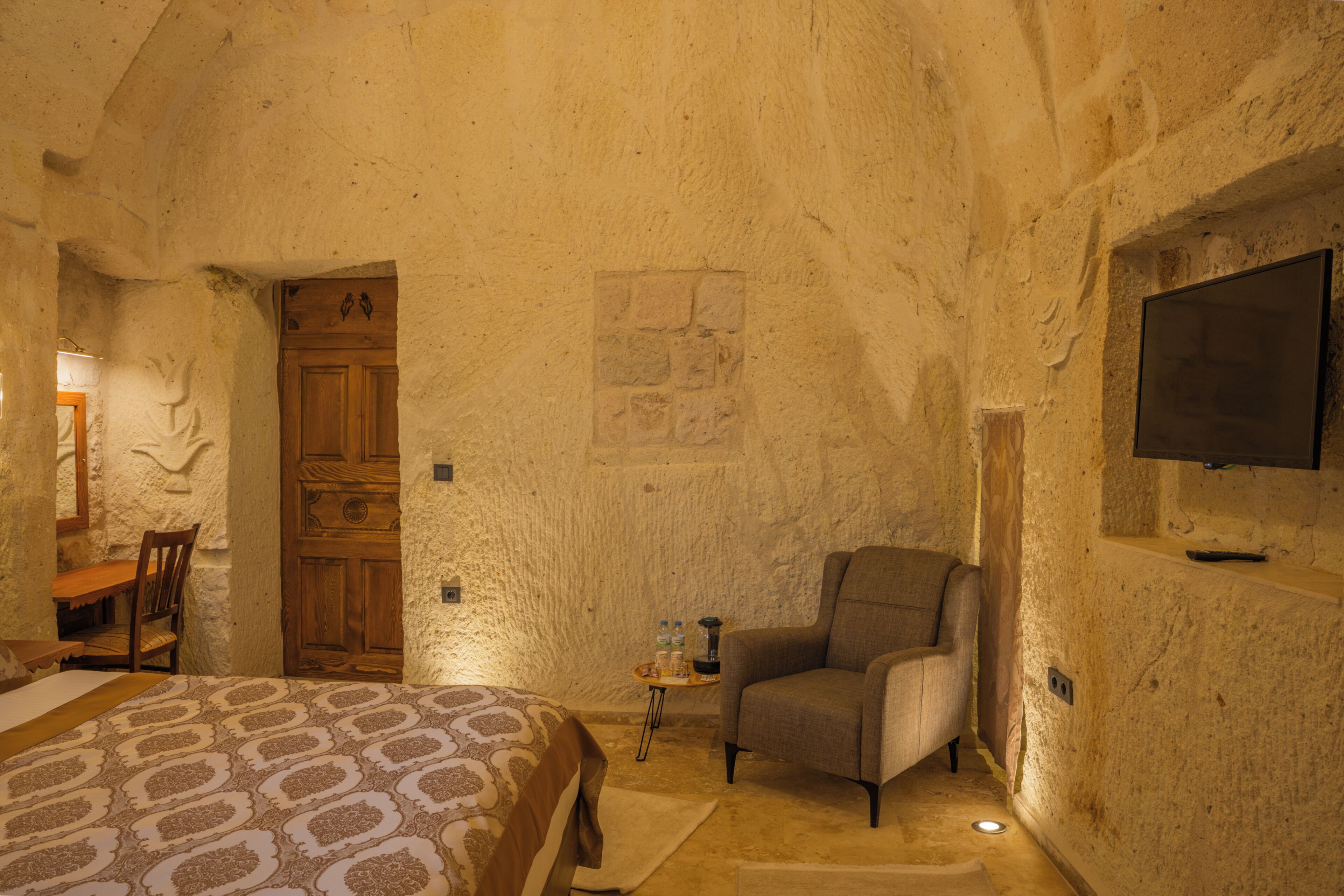 A room with a bed, a chair, a small table with a bottle, and a television mounted on the wall.