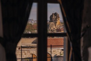 A view through a window with a stone wall and a building with a distinctive rock formation. - Cappa Hisar Cave House (Ortahisar)