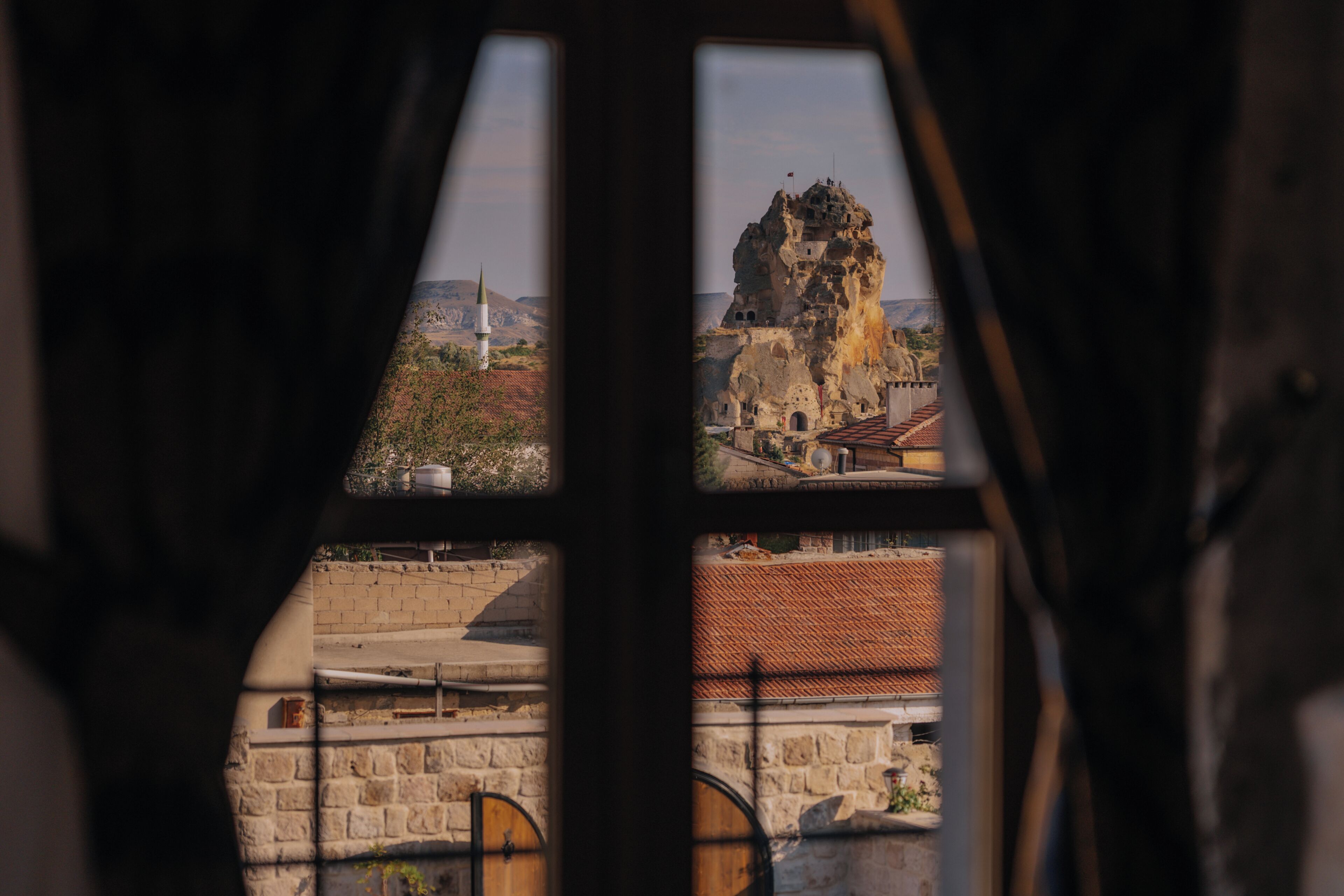 A view through a window with a stone wall and a building with a red roof.