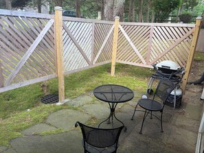 A patio area with a wooden fence, two round tables, and two chairs. - Serene 1-bedroom apartment with AC in East Hampton (East Hampton)