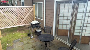 Een terras met een barbecue, twee stoelen en een tafel.