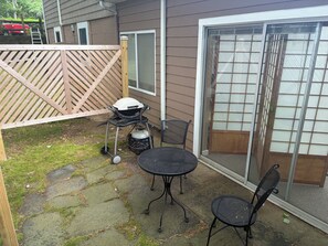 Eine Terrasse mit Grill, zwei Stühlen und einem Tisch.