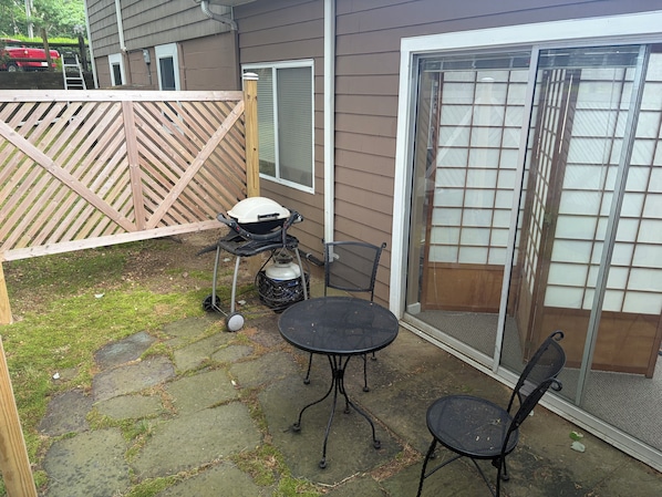 A patio with a grill, two chairs, and a table.