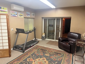 A home office with a treadmill, a large rug, a leather chair, and a desk.