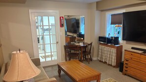 Een woonkamer met een houten tafel, een lamp, een televisie en een keuken op de achtergrond.