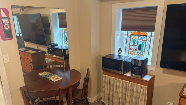 Een eethoek met een houten tafel, stoelen, een boek, een magnetron en een televisie.
