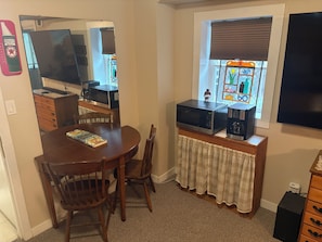 A dining area with a wooden table, chairs, a book, a microwave, and a television.