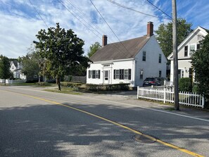 A residential street with houses, a white picket fence, and a clear sky.