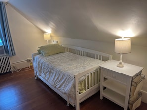A bedroom with a single bed, two bedside lamps, a radiator, and a white nightstand with a lamp.