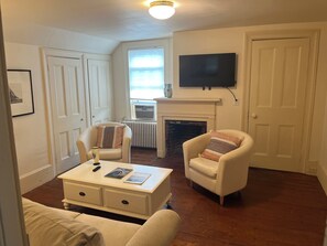 A living room with a fireplace, a television mounted above it, and a window with blinds.