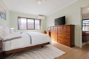 A bedroom with a bed, dresser, TV, and a window. - Charming 3 bedroom, 2 bathroom home Tuart Hill home! Perfectly located between Perth CBD and the coast. Sleeps 6 with a king, double & adjustable single beds plus reverse cycle air-con in every bedroom. Ideal for families, couples and longer stays. (Tuart Hill)