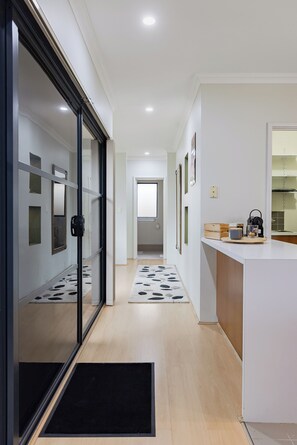 A modern kitchen with a white countertop, a black door, and a hallway leading to a bathroom.